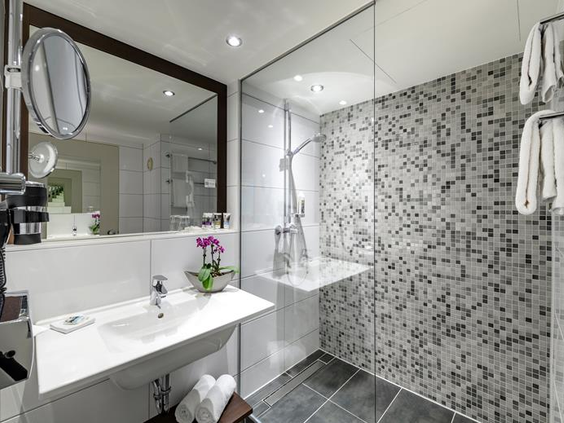 De moderne badkamer van een hotelkamer in Mercure Duisburg City, met een ruime inloopdouche met mozaïektegels en een wastafel.
