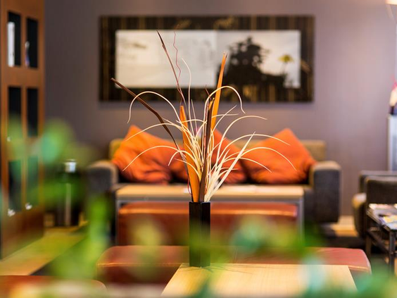 Sfeervol detail van de decoratie in de lounge van het Mercure Hotel Duisburg City, met oranje kussens en een vaas met siertakken.