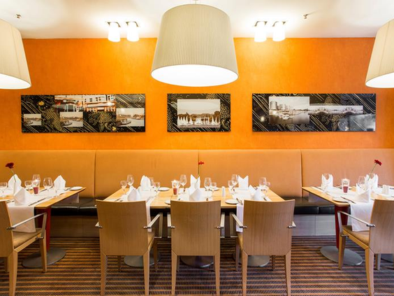Het gezellige en moderne restaurant van het Mercure Hotel Duisburg City, met gedekte tafels en een warme, oranje sfeer.
