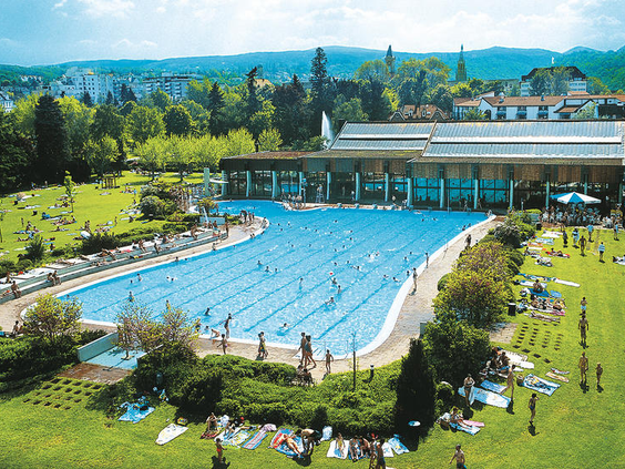 Overzicht van het grote openluchtzwembad Salinarium in Bad Dürkheim, direct naast het Mercure Hotel, met veel mensen die zwemmen en zonnebaden op een zonnige dag.