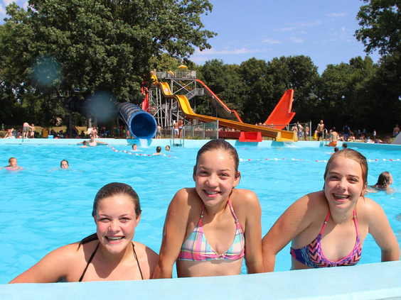Drie lachende meisjes in bikini poseren in het grote buitenzwembad van Waterspeelpark Splesj bij Molecaten Park Bosbad Hoeven.