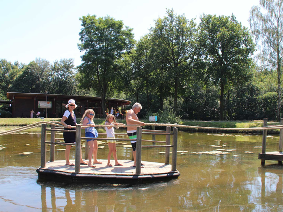 Een gezin met kinderen vaart met het houten trekvlot over de roeivijver op Molecaten Park Bosbad Hoeven.
