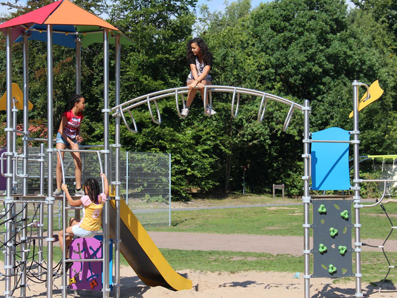 Kinderen klimmen en klauteren op een groot en modern klimrek met een glijbaan en klimwand in de buitenspeeltuin.