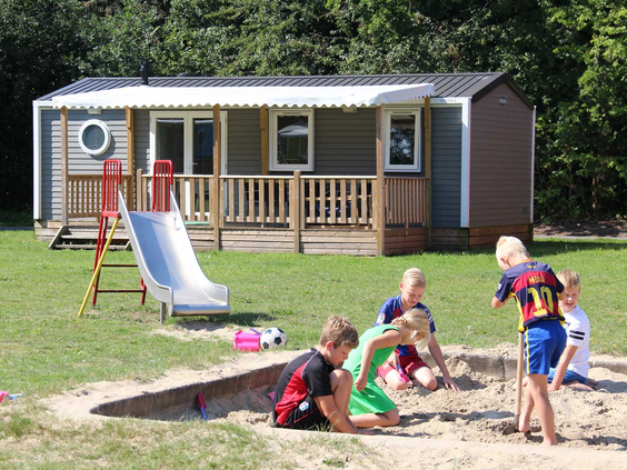 Een groep kinderen speelt samen in een grote zandbak voor hun stacaravan op Molecaten Park Bosbad Hoeven.