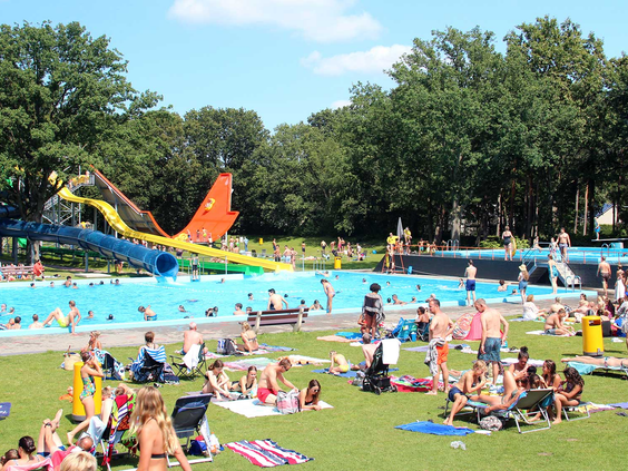 Een grote, zonnige ligweide vol met gezinnen die ontspannen op handdoeken naast de zwembaden van Waterspeelpark Splesj.