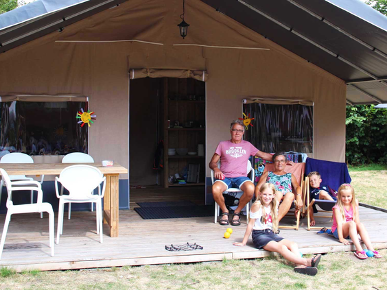 Een gezin ontspant op de veranda van een volledig ingerichte safaritent, een voorbeeld van glamping op Molecaten Park Bosbad Hoeven.
