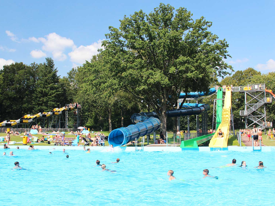 Overzicht van de buitenzwembaden bij Waterspeelpark Splesj met diverse spectaculaire waterglijbanen en volop zwemmende mensen.