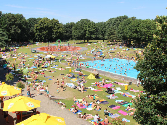 Luchtfoto van het drukbezochte Waterspeelpark Splesj, met een overzicht van de grote ligweide, meerdere zwembaden en gele parasols.