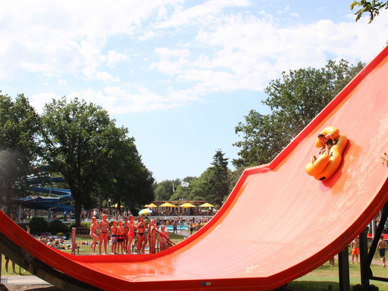 De familieglijbaan 'Waverider' in Waterspeelpark Splesj waar een gezin in een gele band van een brede, rode wildwaterbaan glijdt.