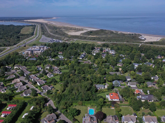 Een luchtfoto die de prachtige ligging van Noordzee Résidence De Banjaard toont, te midden van groen en direct achter de duinen en de Noordzeekust.