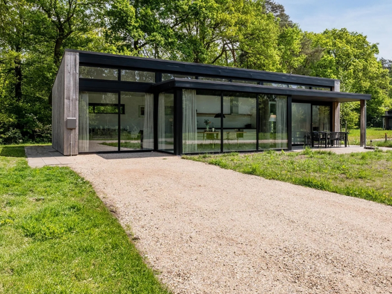 Moderne, zwarte 'Cube' lodge met grote glazen pui op vakantiepark Olde Kottink, gelegen in het groen.