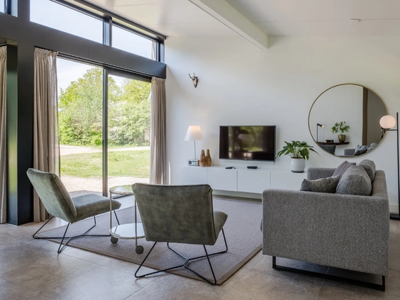 Lichte, moderne woonkamer in een vakantiehuis op Olde Kottink met een comfortabele zithoek en grote ramen met uitzicht op het groen.