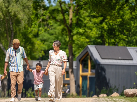 Een familie wandelt hand in hand over vakantiepark Olde Kottink, met de lodges op de achtergrond.