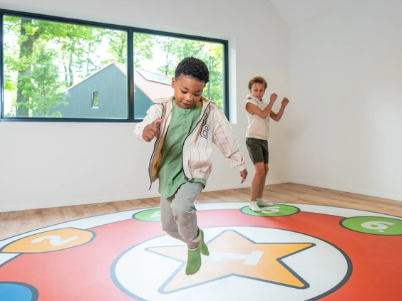 Twee jongens spelen een interactief spel op een grote, kleurrijke speelvloer in de indoor speelruimte van vakantiepark Olde Kottink.