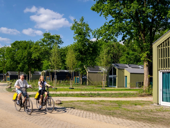 Een gezin fietst vrolijk over een pad op vakantiepark Olde Kottink, langs de moderne vakantielodges.