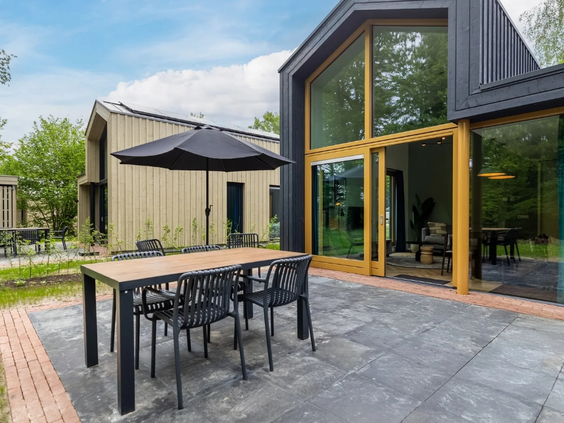 Het ruime terras van een moderne vakantielodge op Olde Kottink, met een buitentafel, stoelen en uitzicht op de natuur.