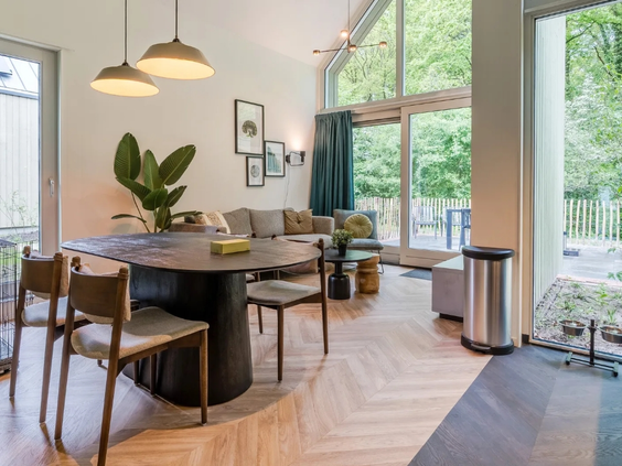 Stijlvol interieur van de woon- en eetkamer in een lodge op vakantiepark Olde Kottink, met grote ramen en uitzicht op de natuur.