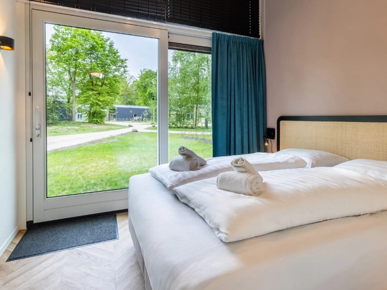 Slaapkamer in een lodge op Olde Kottink met een opgemaakt bed en een deur die direct toegang geeft tot de tuin.