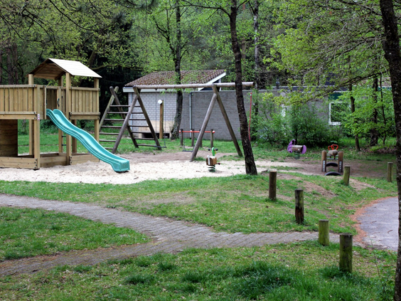 Speeltuin met een glijbaan, schommels en een wipkip, omringd door groen gras en bomen op Parc de Berkenhorst.