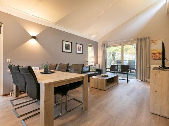 Ruime en lichte woonkamer met een grote eettafel en een comfortabele zithoek in een bungalow op Parc de Berkenhorst.