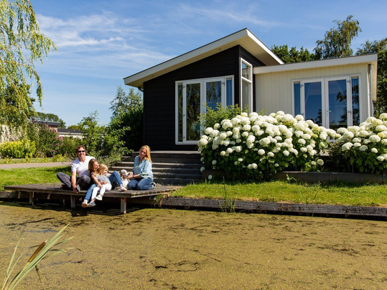 Een gezin zit gezellig samen op een aanlegsteiger aan het water voor hun moderne vakantiehuisje op Parc de IJsselhoeve.