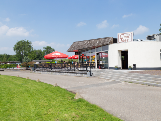 Het zonnige terras met rode parasols van eetcafé 'Geen Idee' op Parc de IJsselhoeve, gelegen aan het water.