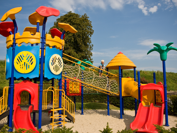 Een groot en kleurrijk speelkasteel met glijbanen, een klimwand en een touwbrug in de zandspeeltuin van Parc de IJsselhoeve.