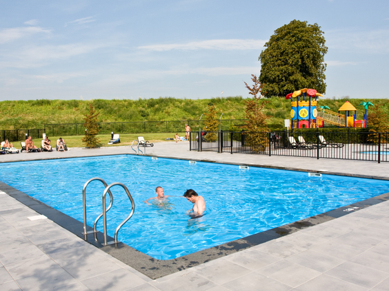 Het verwarmde buitenzwembad met een apart peuterbad en een speeltuin op de achtergrond, op een zonnige dag op Parc de IJsselhoeve.