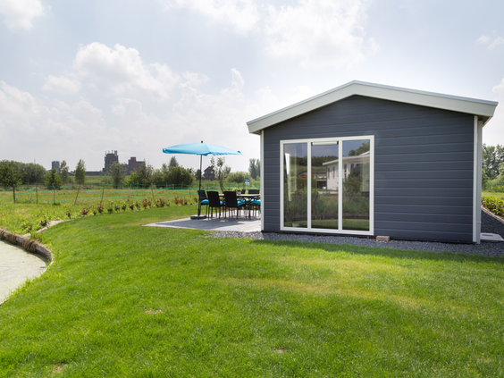 Een modern grijs vakantiehuisje met een groot groen grasveld en een terras met parasol op Parc de IJsselhoeve.