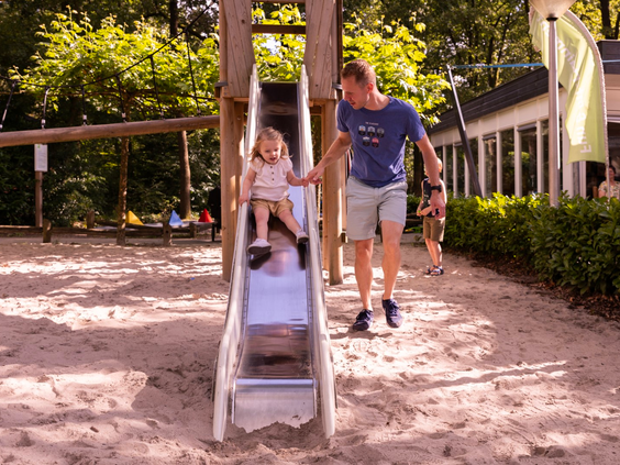 Een vader helpt zijn jonge dochter van de glijbaan af in de buitenspeeltuin van Parc Heihaas.