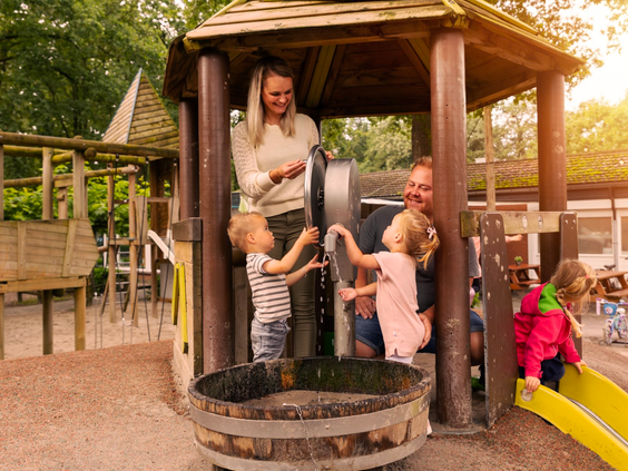 Een gezin met jonge kinderen speelt samen bij de waterpomp in de avontuurlijke houten speeltuin van Parc Heihaas.