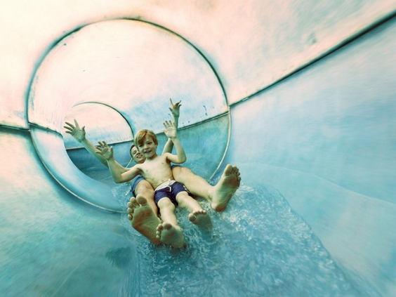 Een jongen glijdt met zijn armen in de lucht met hoge snelheid door een doorzichtige waterglijbaan in het zwemparadijs Aqua Mundo van Center Parcs Park Allgäu.