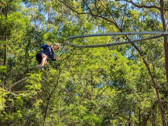 Een jongen vliegt met een veiligheidsharnas aan een hangende achtbaan, de Zip Coaster, door de groene bossen van Park Allgäu.