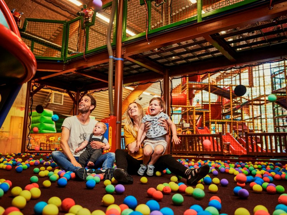 Een gelukkig gezin met een baby en een peuter zit te midden van de gekleurde ballen in de ballenbak van de BALUBA binnenspeeltuin in Center Parcs Park Allgäu.