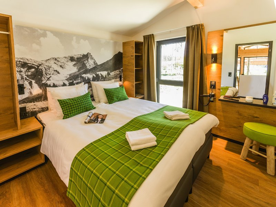 Een nette slaapkamer in een Comfort cottage van Park Allgäu, met een opgemaakt tweepersoonsbed met groene sprei en een fotowand van een berglandschap.