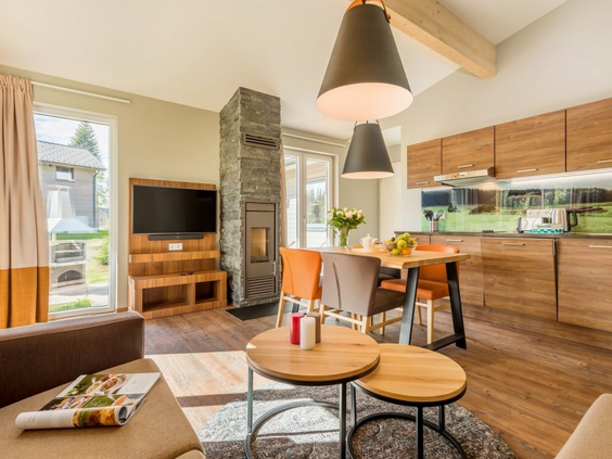 De zeer luxe en modern ingerichte woonkamer en open keuken van een Exclusive cottage in Park Allgäu, voorzien van een design haard, eethoek en houten details.