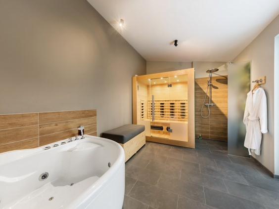 De luxe wellnessbadkamer van een VIP of Exclusive cottage in Park Allgäu, uitgerust met een groot bubbelbad, een privé-infraroodsauna en een regendouche.