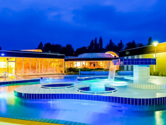 De sfeervol verlichte thermaalbaden van Roompot Klein Vink in de avond, met blauwe en gele lampen onder water.