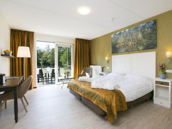 Lichte en ruime comfort hotelkamer met opgemaakt bed en open deuren naar het balkon bij Roompot Klein Vink.