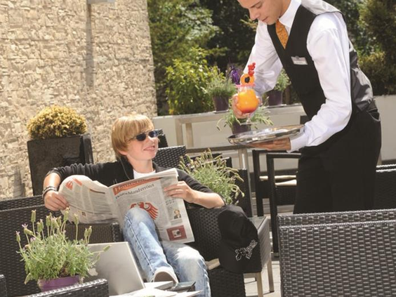 Gast ontspant met een krantje en een drankje op het zonnige terras van het kindvriendelijke Parkhotel Oberhausen.