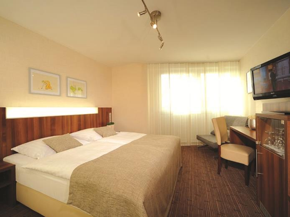 Een comfortabele en lichte hotelkamer in Parkhotel Oberhausen, met een groot bed en een gezellig zitje bij het raam.