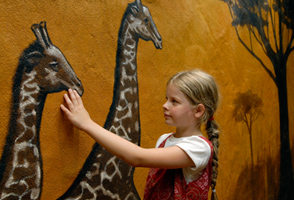 Meisje met vlechten raakt een muurschildering van giraffen aan in het Afrikaans gethematiseerde Hotel Matamba in Phantasialand.