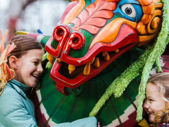 Twee lachende kinderen knuffelen een entertainer in een groot, kleurrijk Chinees drakenkostuum in themagebied China Town in Phantasialand.