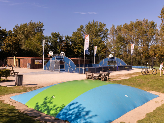 Een grote, kleurrijke airtrampoline voor kinderen om op te springen bij Vakantiepark Port Greve, met een sportkooi in de achtergrond.