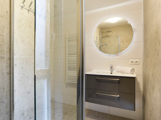 De stijlvolle en moderne badkamer in een vakantiehuis op Port Greve, met een ruime inloopdouche en een wastafel met een ronde, verlichte spiegel.