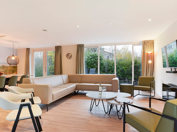 De ruime, licht ingerichte woonkamer van een vakantiehuis op Port Greve met een grote hoekbank, eettafel en uitzicht op de tuin.