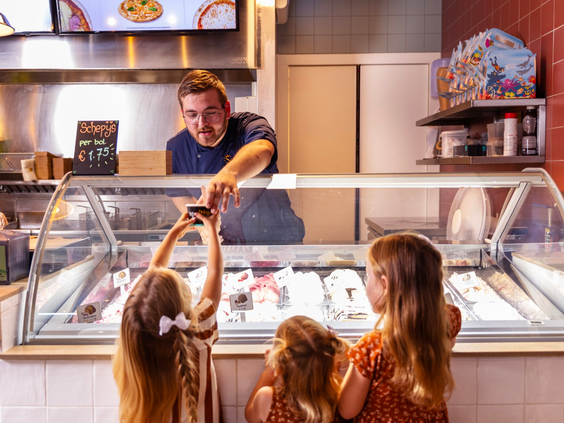 Drie meisjes staan bij de ijsvitrine van de snackbar op Vakantiepark Port Greve en krijgen een ijsje van een medewerker.