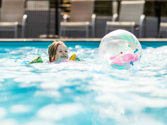 Jong meisje met zwemvleugels speelt met een opblaasbare bal in het blauwe water van het buitenzwembad op Recreatiepark Beekbergen.
