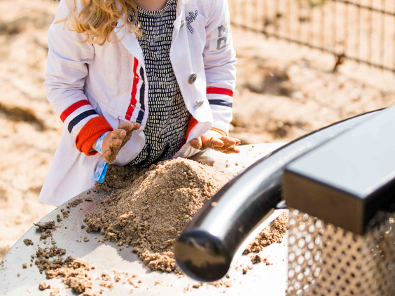 Een meisje is aan het spelen met een zand- en watertafel in de speeltuin, waar ze zand door een trechter laat gaan.