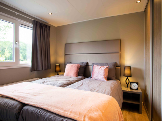 De stijlvol ingerichte tweepersoonsslaapkamer met opgemaakte bedden in een luxe chalet op Recreatiepark Beekbergen.